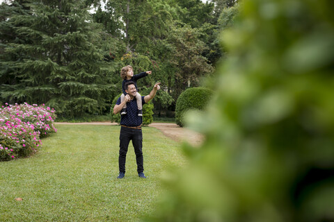 Vater mit Sohn auf den Schultern im Park, die mit den Fingern zeigen, lizenzfreies Stockfoto