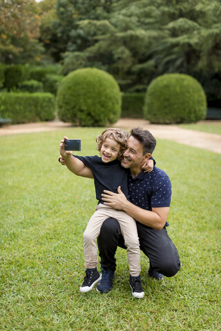 Glücklicher Vater und Sohn bei der Aufnahme eines Selfies im Park, lizenzfreies Stockfoto
