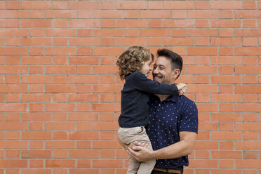 Happy father carrying son at brick wall - MAUF02092