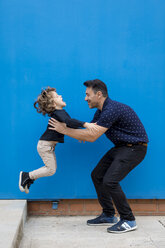 Happy father playing with son at blue wall - MAUF02094