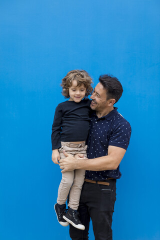 Glücklicher Vater mit Sohn an der blauen Wand, lizenzfreies Stockfoto