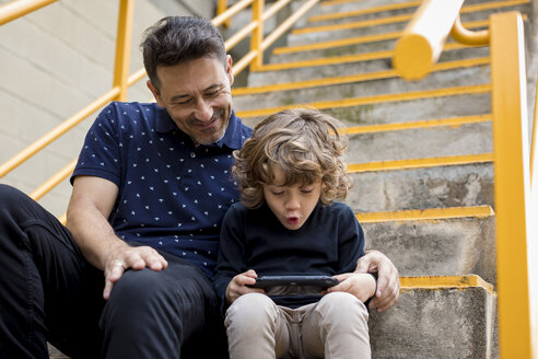 Father watching son playing with handheld game console - MAUF02098