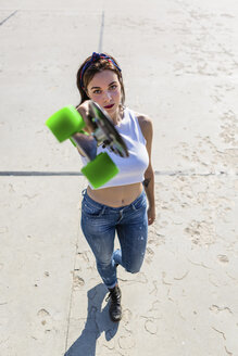 Porträt einer jungen Frau, die ein Skateboard hochhält - MGIF00265