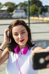 Porträt einer lächelnden jungen Frau mit Kopfhörern und Mobiltelefon in der Stadt - MGIF00278