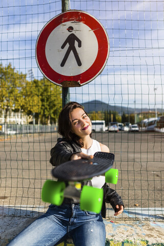 Porträt einer lächelnden jungen Frau mit Skateboard, lizenzfreies Stockfoto