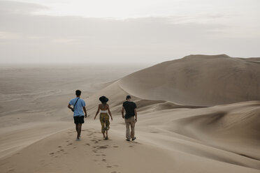Namibia, Namib, Rückenansicht von drei Freunden, die Seite an Seite auf einer Wüstendüne spazieren gehen - LHPF00274
