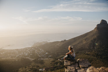Südafrika, Kapstadt, Kloof Nek, Frau sitzt bei Sonnenuntergang auf einem Felsen - LHPF00291