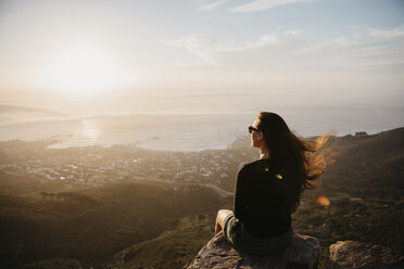 Südafrika, Kapstadt, Kloof Nek, Frau sitzt bei Sonnenuntergang auf einem Felsen - LHPF00293