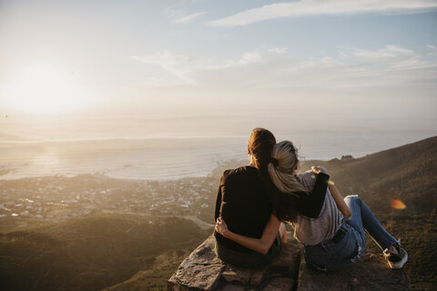 Südafrika, Kapstadt, Kloof Nek, zwei Frauen sitzen bei Sonnenuntergang auf einem Felsen, lizenzfreies Stockfoto