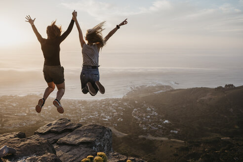 Südafrika, Kapstadt, Kloof Nek, zwei Frauen springen bei Sonnenuntergang auf einen Felsen - LHPF00296