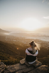 Südafrika, Kapstadt, Kloof Nek, Frau sitzt bei Sonnenuntergang auf einem Felsen - LHPF00298