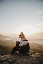 Südafrika, Kapstadt, Kloof Nek, lächelnde Frau sitzt bei Sonnenuntergang auf einem Felsen - LHPF00299