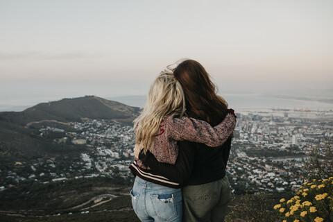 Südafrika, Kapstadt, Kloof Nek, Rückansicht von zwei sich umarmenden Frauen bei Sonnenuntergang, lizenzfreies Stockfoto