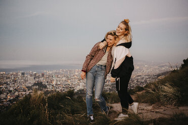 South Africa, Cape Town, Kloof Nek, two happy women embracing at sunset with cityscape in background - LHPF00309
