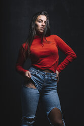 Porträt einer jungen Frau mit Tätowierung auf dem Oberschenkel, die vor einem schwarzen Hintergrund posiert - DAMF00008