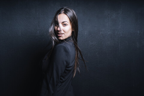 Porträt einer jungen Frau mit schwarzem Blazer vor einem schwarzen Hintergrund, lizenzfreies Stockfoto