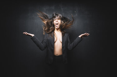 Portrait of young woman screaming and tossing her hair in front of black background - DAMF00023