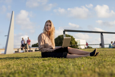 Young businesswoman sitting on a meadow using laptop - MAUF02114