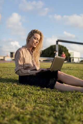 Junge Geschäftsfrau sitzt auf einer Wiese und benutzt einen Laptop, lizenzfreies Stockfoto