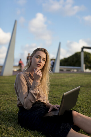 Junge Geschäftsfrau sitzt auf einer Wiese und benutzt einen Laptop, lizenzfreies Stockfoto