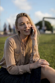 Lächelnde junge Geschäftsfrau am Handy auf einer Wiese - MAUF02118