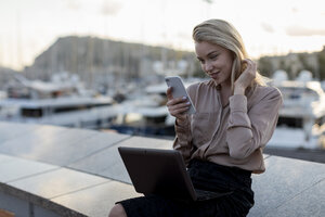 Schöne junge Geschäftsfrau mit Handy und Laptop an der Waterfront - MAUF02127