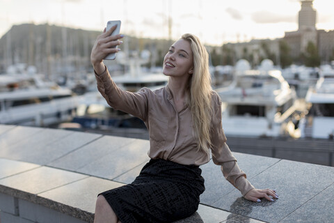 Lächelnde junge Frau macht ein Selfie am Wasser, lizenzfreies Stockfoto