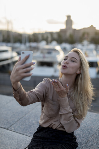 Junge Frau macht ein Selfie und gibt einen Kuss am Wasser, lizenzfreies Stockfoto