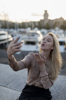 Junge Frau macht ein Selfie und gibt einen Kuss am Wasser - MAUF02129