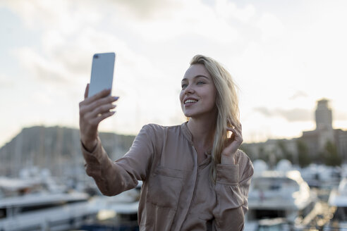 Lächelnde junge Frau macht ein Selfie am Wasser - MAUF02130