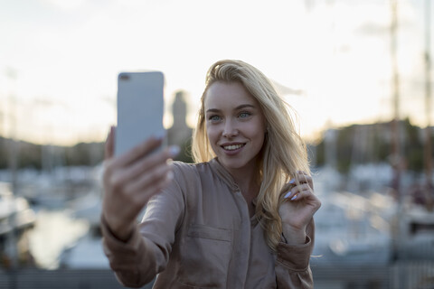 Lächelnde junge Frau macht ein Selfie am Wasser, lizenzfreies Stockfoto