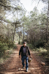 Porträt eines lächelnden älteren Mannes, der mit einem Korb voller Pilze im Wald spazieren geht - JRFF02251