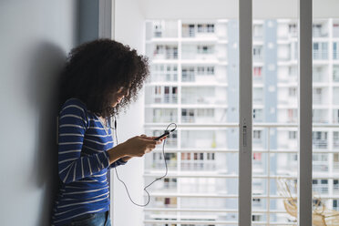 Young woman using smartphone and earphones at home - KKAF03075