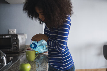 Young woman pouring water into a mug in her kitchen - KKAF03080