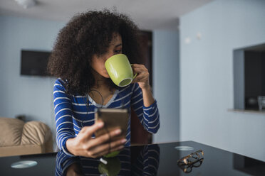 Junge Frau trinkt Kaffee und schaut auf ihr Handy - KKAF03083