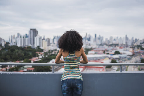 Panama, Panama City, back view of young woman standing on balcony looking at view - KKAF03100