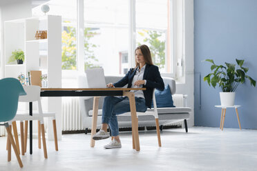 Young businesswoman sitting in office, using laptop - GUSF01674