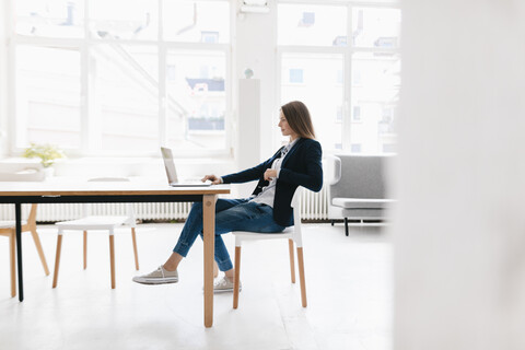 Junge Geschäftsfrau sitzt im Büro und benutzt einen Laptop, lizenzfreies Stockfoto