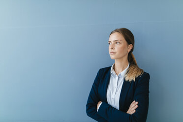 Porträt einer jungen, skeptisch dreinblickenden Geschäftsfrau vor blauem Hintergrund - GUSF01687