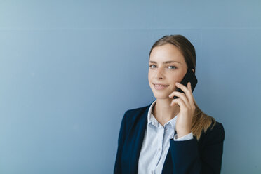 Porträt einer jungen Geschäftsfrau vor blauem Hintergrund, die mit ihrem Smartphone spricht - GUSF01688