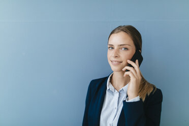 Portrait of a young businesswoman against blue background, talking on her smartphone - GUSF01688