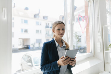 Young businesswoman standing at the window, using digital tablet - GUSF01690