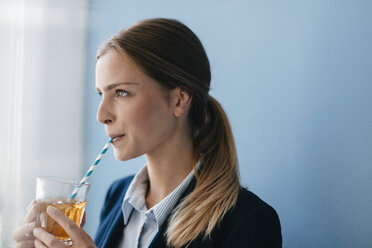 Portrait of a young businesswoman against blue background, drinking iced tea with a straw - GUSF01692