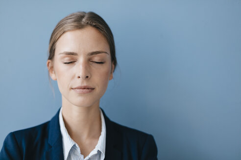 Porträt einer jungen Geschäftsfrau vor blauem Hintergrund, die sich mit geschlossenen Augen entspannt - GUSF01696