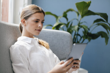 Junge Frau sitzt auf der Couch und benutzt ein digitales Tablet - GUSF01701