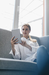 Junge Frau sitzt auf der Couch und benutzt ein digitales Tablet - GUSF01702