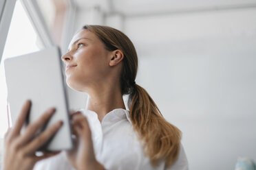 Young businesswoman standing at the window, usind digital tablet - GUSF01708