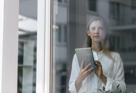 Junge Geschäftsfrau, die am Fenster steht und ein digitales Tablet benutzt, lizenzfreies Stockfoto