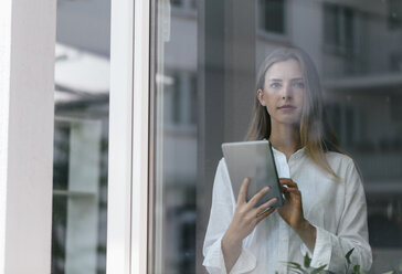 Young businesswoman standing at the window, using digital tablet - GUSF01711