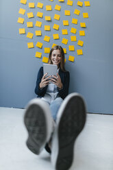 Young businesswoman sitting under data cloud, using digital tablet - GUSF01719